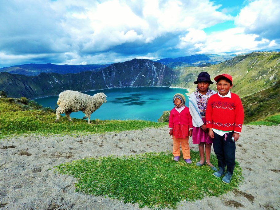 Local kids stop for a photo in front of the piercing blue water of Quilotoa Lake