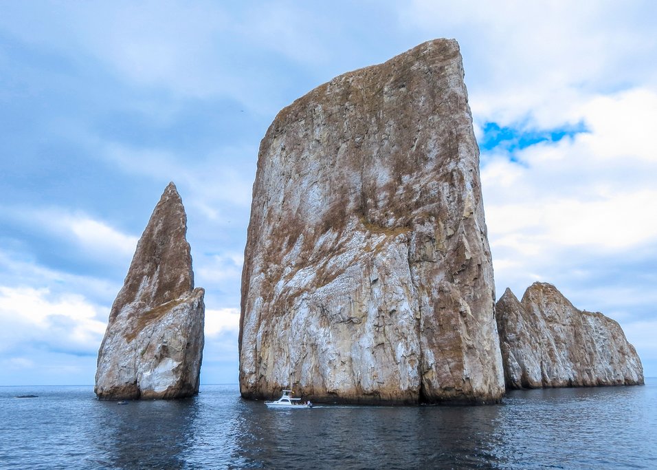 Kicker Rock, a massive rock formation, dwarfs a passing boat