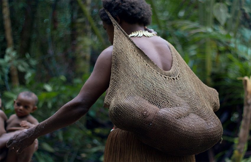 A Dani woman is carrying her baby inside a string bag called 'Noken'