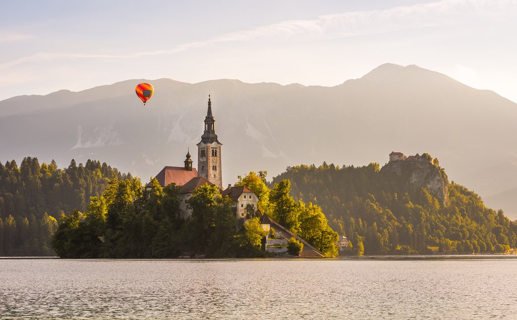 Hot air balloon flies over Lake Bled, Pilgrimage church, and Bled Castle in the background