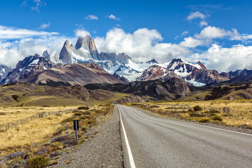 A road in the foreground leads to the Fitz Roy Mountains in the background