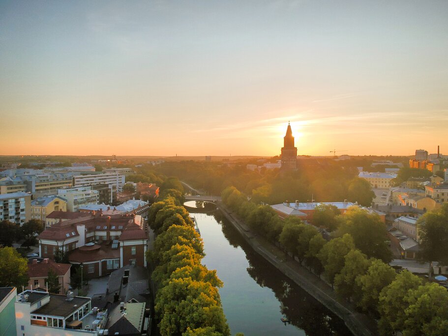 Aerial view of Turku at sunrise. The sun shines from behind a cathedral and the Aura River flows through the middle of the scene