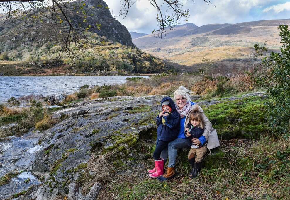 Woman and two little children smile in Killarney Ireland at a stop along the ring of Kerry overlooking a scenic lake and mountain background