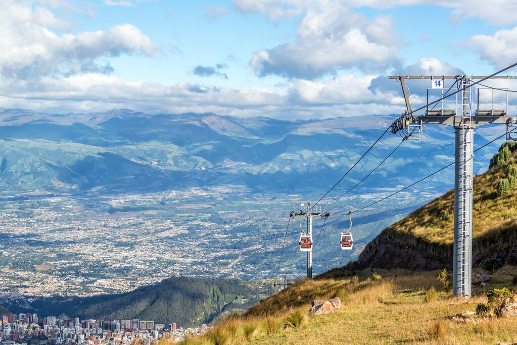 Quito cable car El Teleférico rises up the side of a grassy mountain with the city visible in the distant background