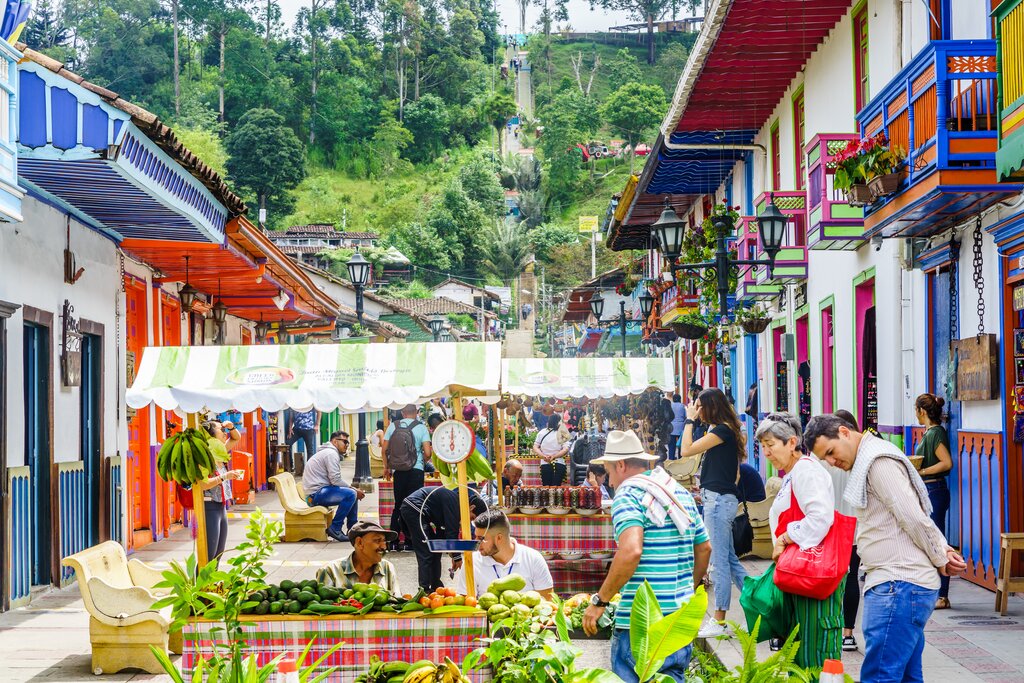 A colorful street market with a lush backdrop