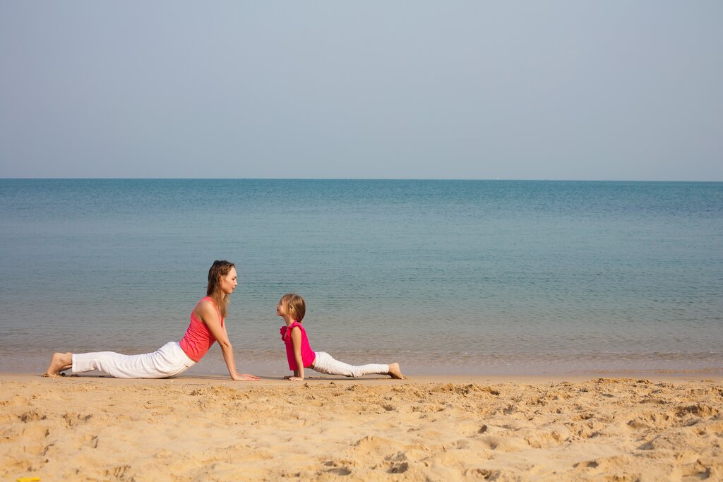Mother and daughter do yoga on the beach