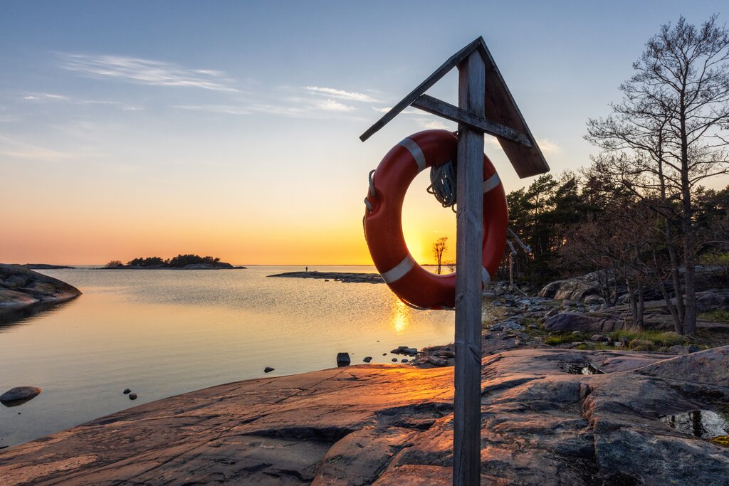 View of the sunset from the rocky shore of Porkkalaniemi with a post holding an emergency float in the midground