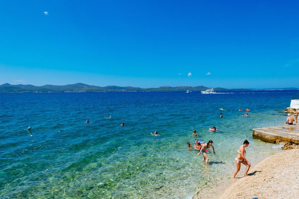 Beachgoers wade in the crystalline waters of the Adriatic Sea near Zadar