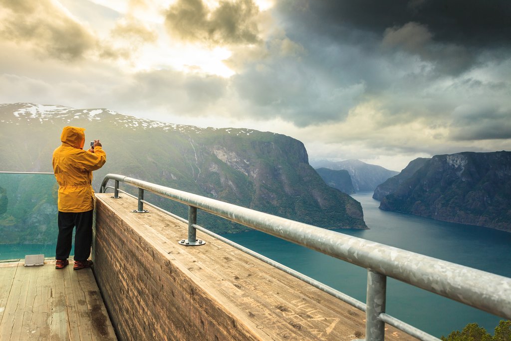 Male tourist nature photographer taking photo with camera enjoying Aurland fjord landscape from Stegastein lookout Norway Scandinavia.