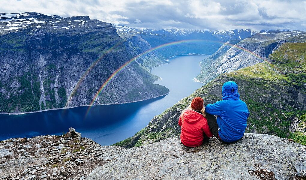 Couple sits on rock and looks at mountains near Trolltunga. Popu