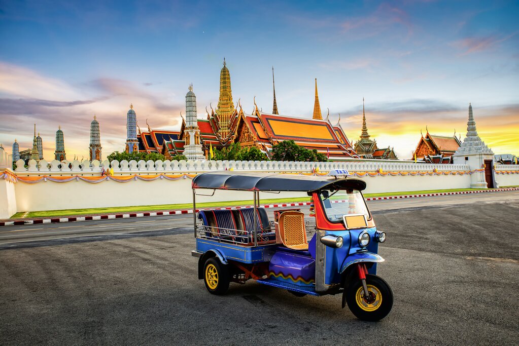 A tuk-tuk in front of a golden temple at dusk