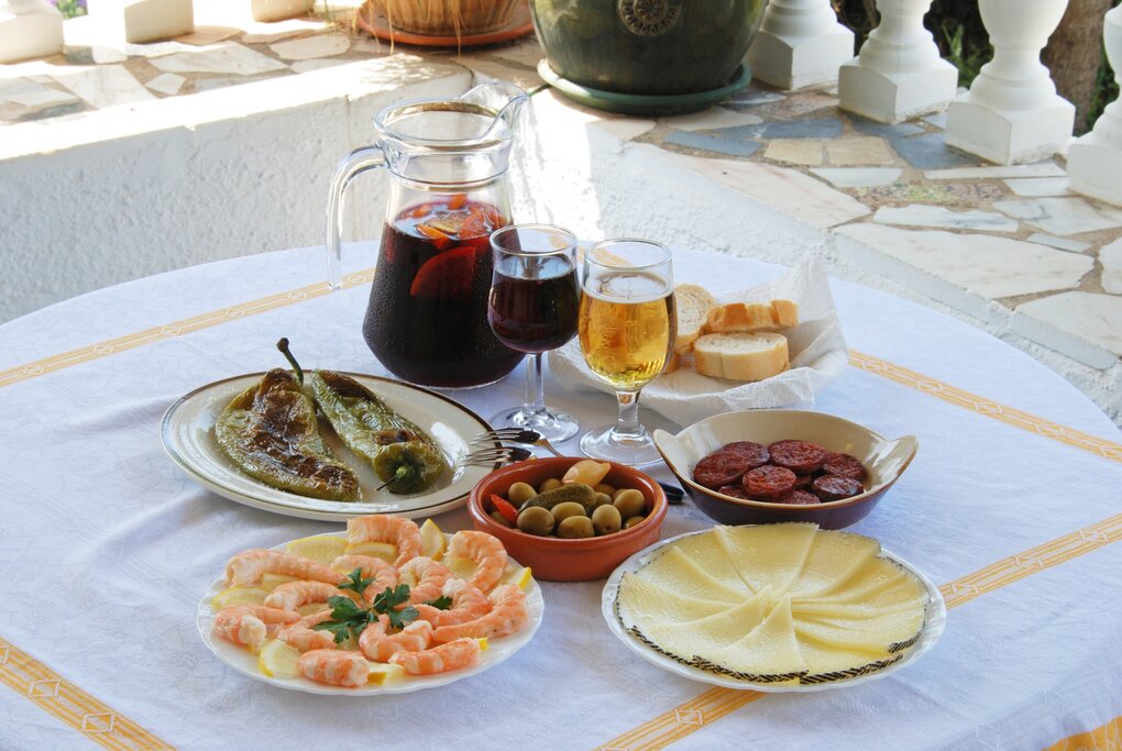 A selection of tapas with sangria and beer, Fried green peppers, olive cocktail, Chorizo slices, Sliced Manchego cheese, Prawns,