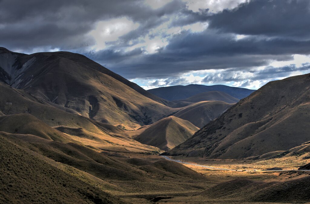Aerial view of Lindis Pass, South Island, NZ. Spots of sunshine make the rolling golden hills glow