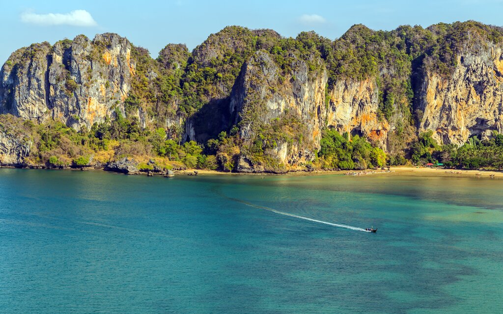 Aerial photo of Railay Beach with clear water in the foreground and a row of limestone karst cliffs covered in vegetation in the background