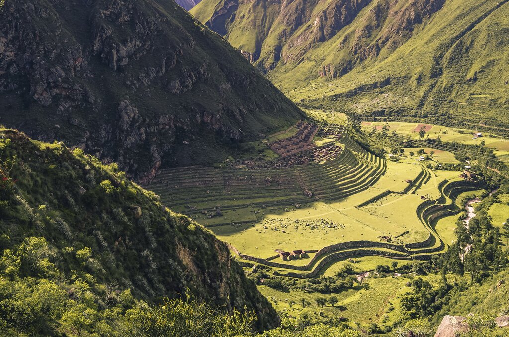 Aerial distant view of Llactapata ruins, made up of curving terraces on the valley floor between high mountains