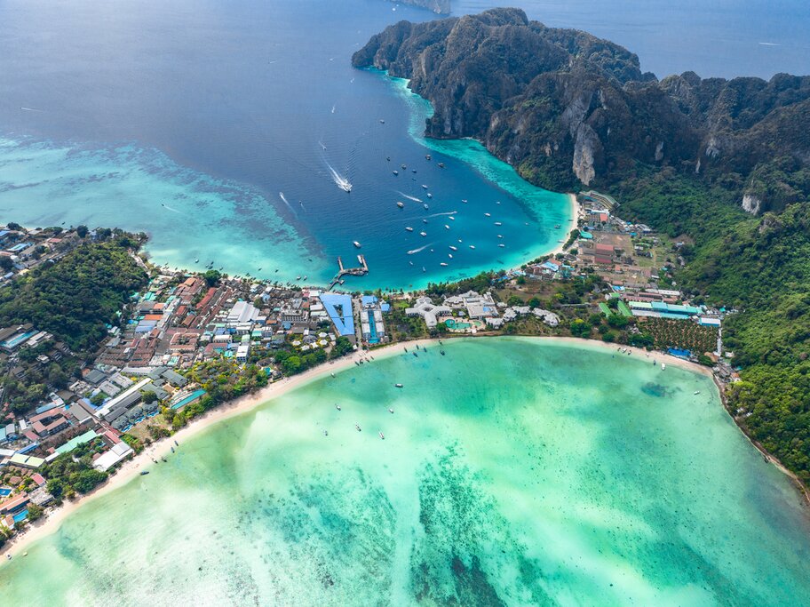 Aerial photo over Koh Phi Phi Don with two bays on either side of a narrow strip of land. Loh Dalum Bay is closer to the viewer and Ton Sai Beach is farther away