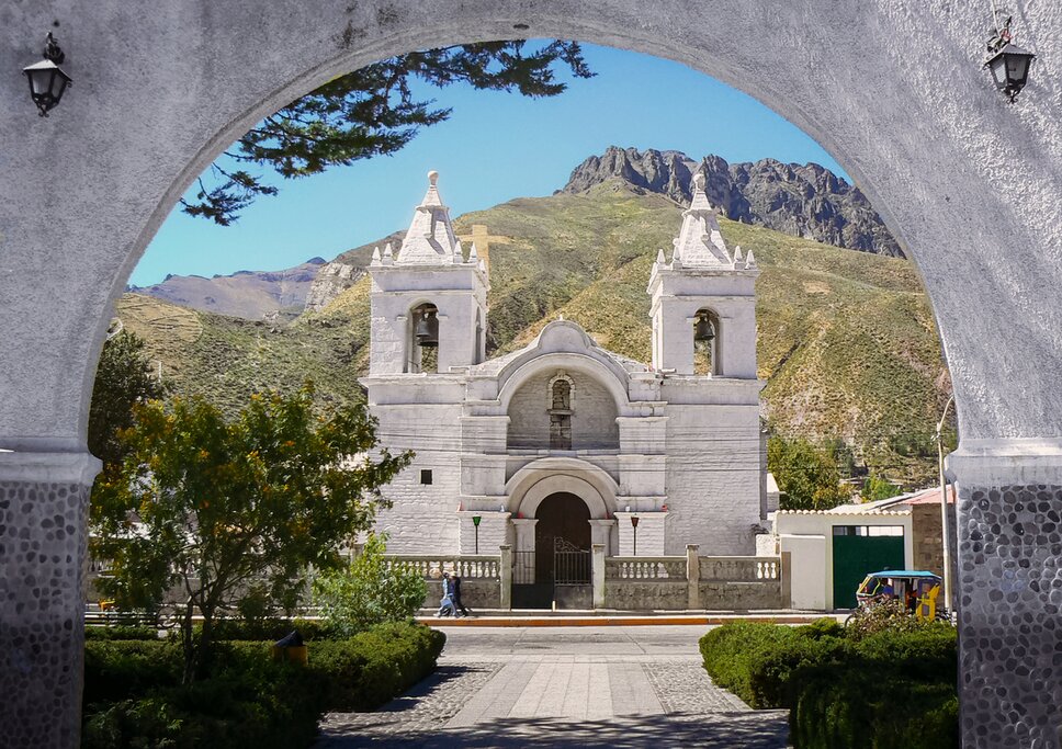 View of a white stone church in Chivay, Peru, seen through an archway of white plaster and gray river rocks
