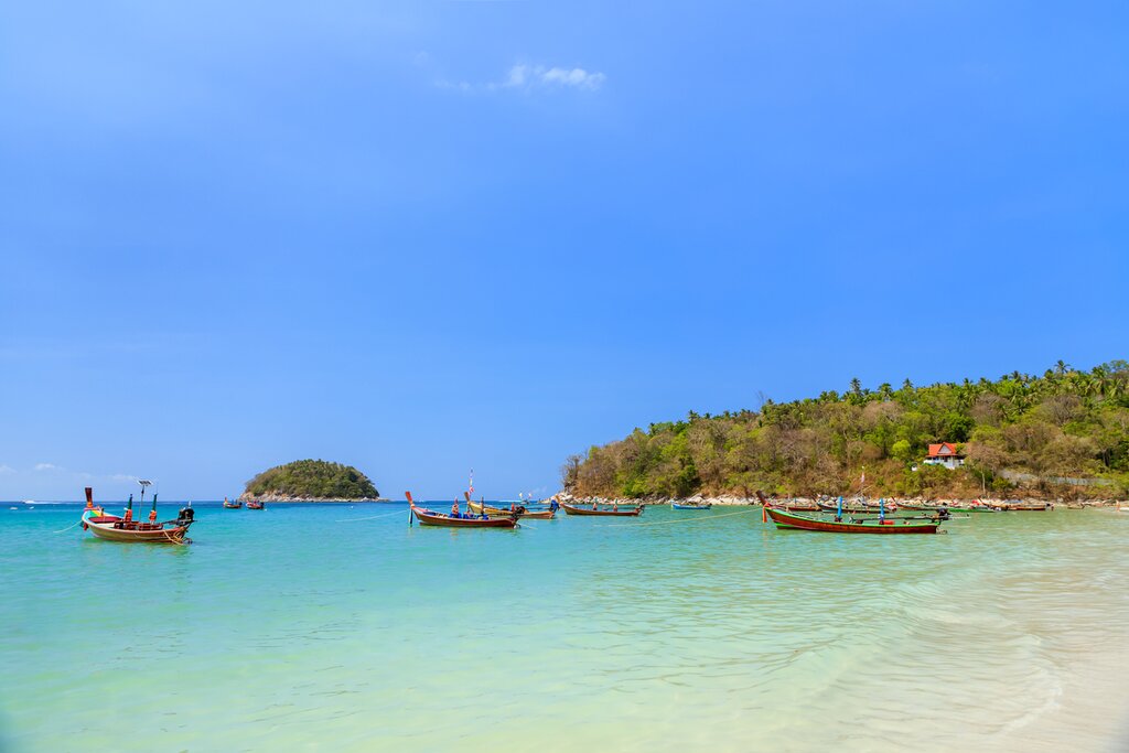 Photo of Kata Beach on Phuket, with calm, turquoise water and several long-tail boats docked in the water