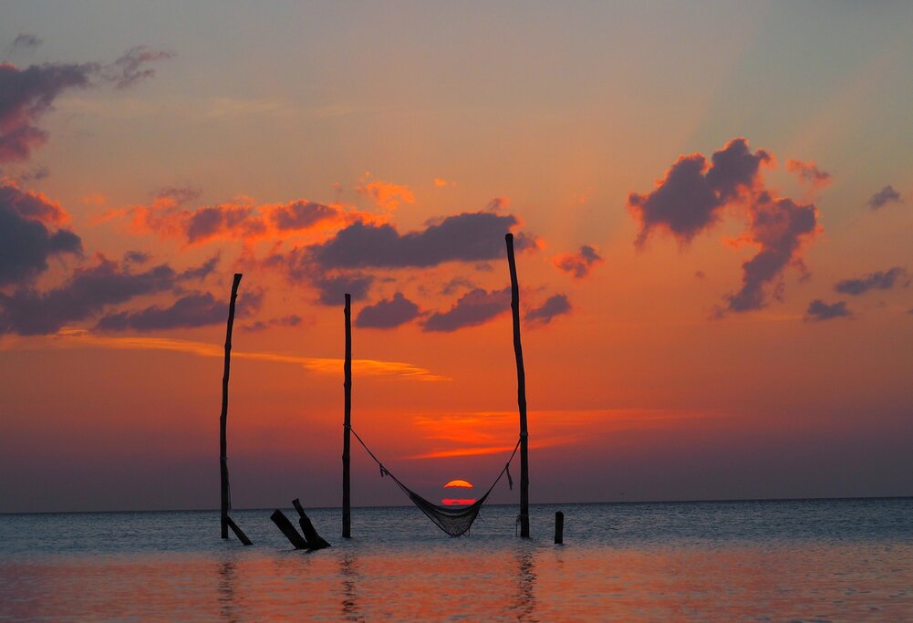 a hammock supported by two beams in the shallow ocean during a pink sunset in Holbox