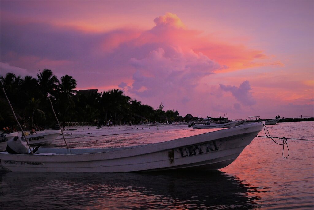 A boat in the water of Holbox at sunset with billowing pink clouds