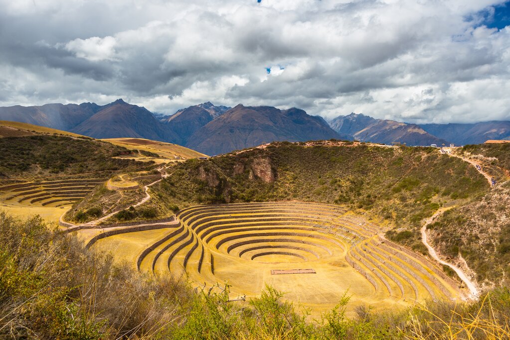 Wide angle view of the glowing majestic concentric terraces of Moray, supposed Inca's laboratory in Sacred Valley, major travel destination in Cusco region, Peru. Dramatic cloudy sky.