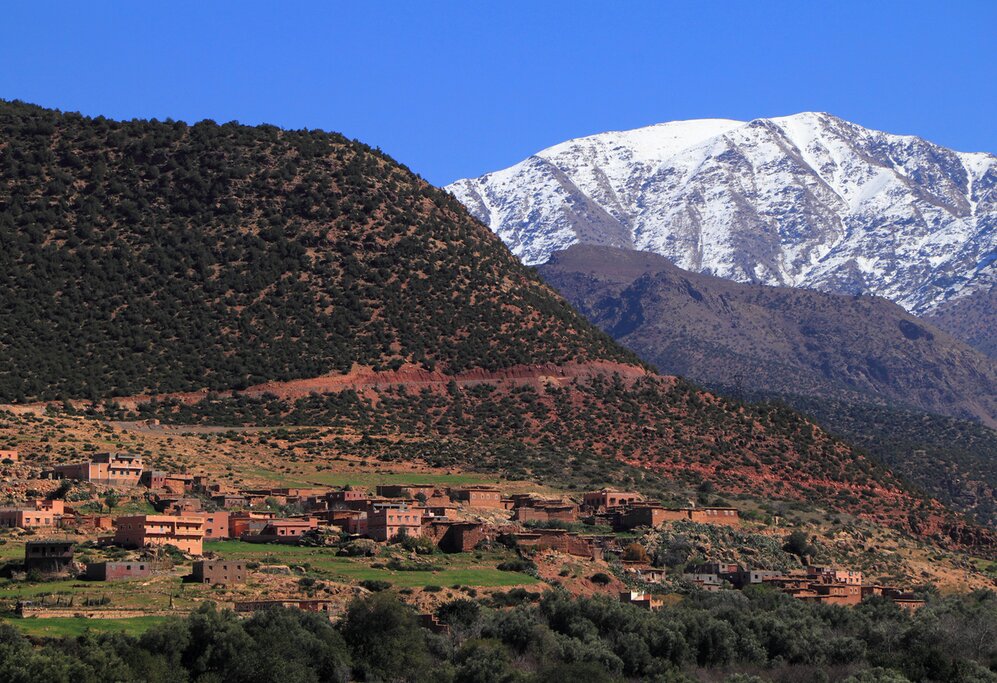Snowcapped peaks and fertile valley with a small village built of adobe, High Atlas Mountain range in the Toubkal National Park.