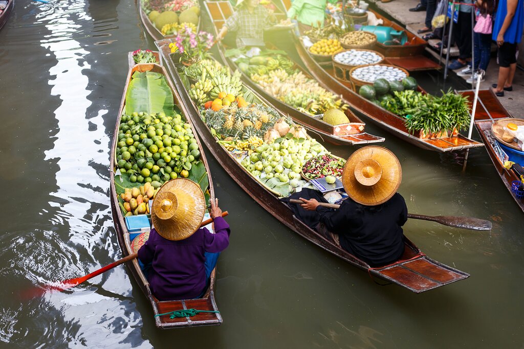 Photo of Damnoen Saduak Floating Market focused on two boats full of fruit captained by women in straw hats, taken from above and behind