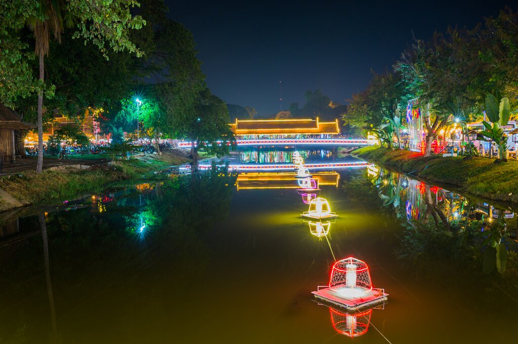 Photo of the Siem Reap River looking toward a bridge at night. The bridge is lit up with brightly colored neon lights, and lighted cubes float in the water
