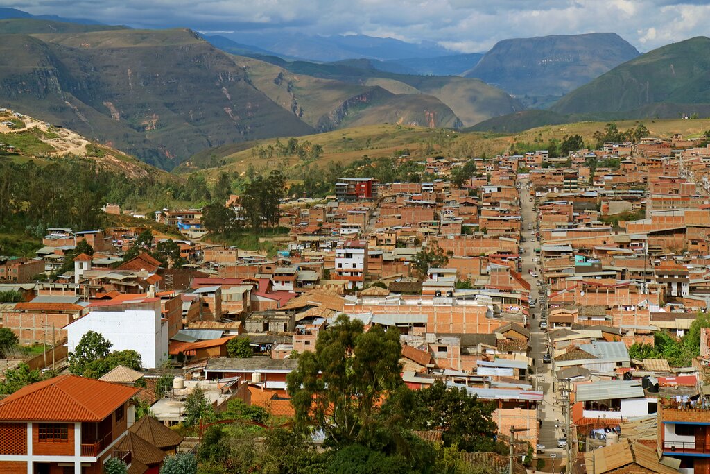 View of Chachapoyas from the Luya Urco viewpoint above the town with terracotta-colored rooftops, a central street extending away from the camera, and green mountains in the background