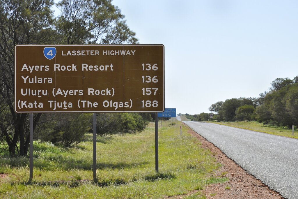 Sign on Lasseter Highway describing distances to Ayers Rock Resort, Yulara, Uluru (Ayers Rock), and Kata Tjuta (The Olgas)