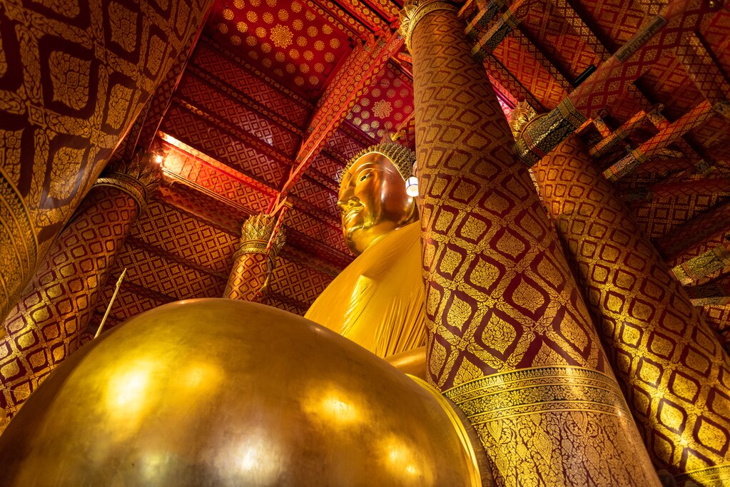 Photo looking up from the foot of a 57-foot-tall seated golden Buddha statue. An ornate red and gold ceiling is visible in the background.