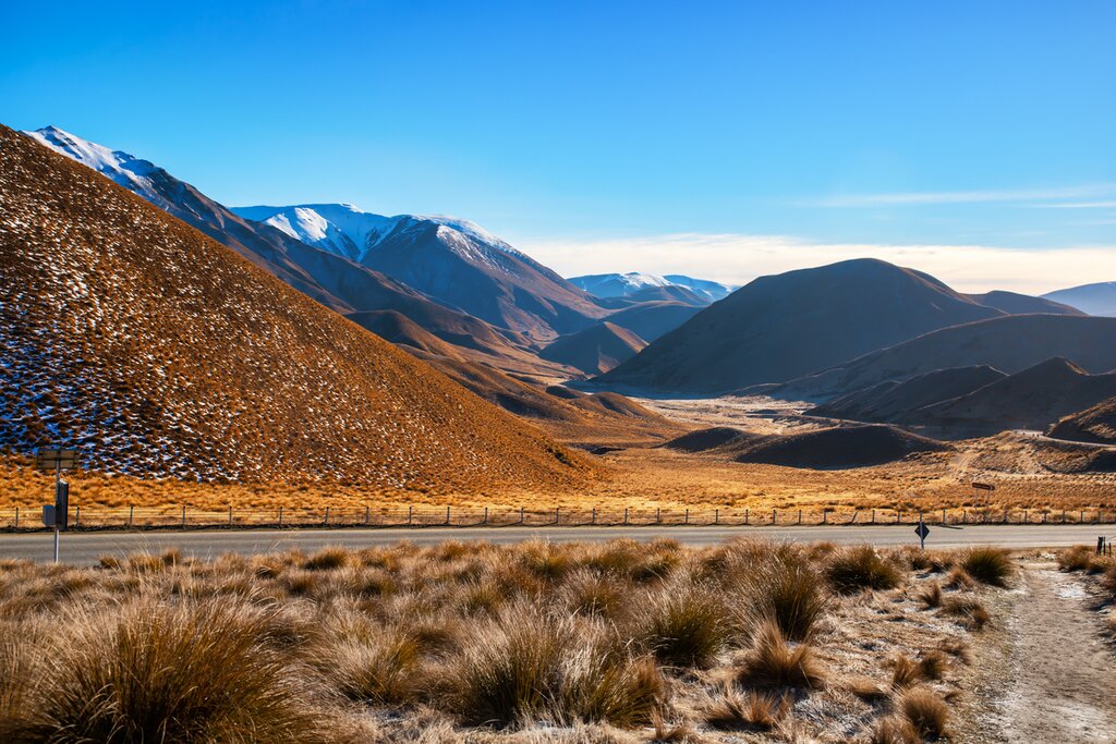 A landscape view of a road through the Lindis Pass with golden brown, snow-dusted hills in the distance