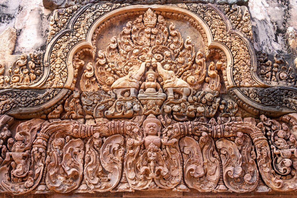 Photo of a highly detailed, intricate bas relief of Hindu symbols carved into red sandstone at Banteay Srei Temple