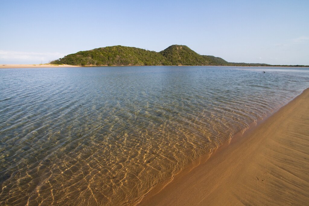 Clear water at the shore of the mouth of Kosi Bay with a green island in the background