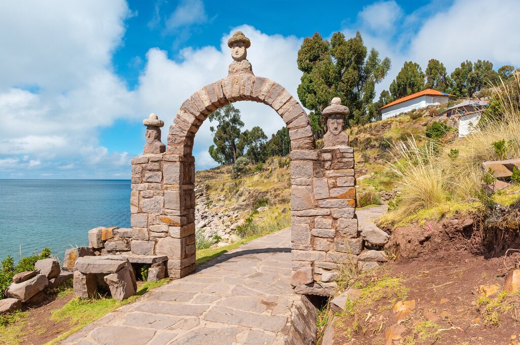 The Arch of the Elder on Taquile Island. Lake Titicaca is visible on the left, and in the center of the image stands the arch topped with three busts wearing bowler-style hats
